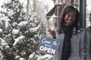 black-woman-standing-outside-store-in-snow-with-we're-open-sign